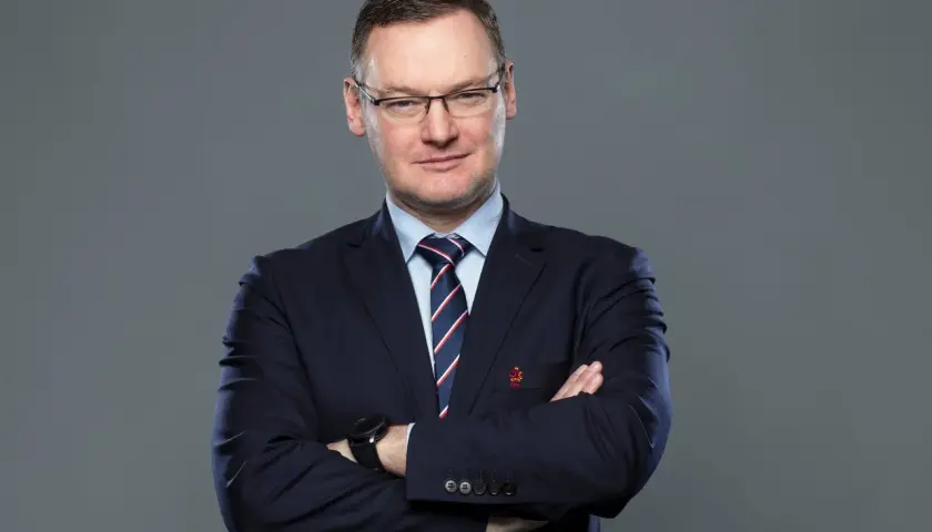 Miłosz Stępiński w granatowym garniturze, z rękami skrzyżowanymi na piersi, patrzy pewnie w obiektyw.