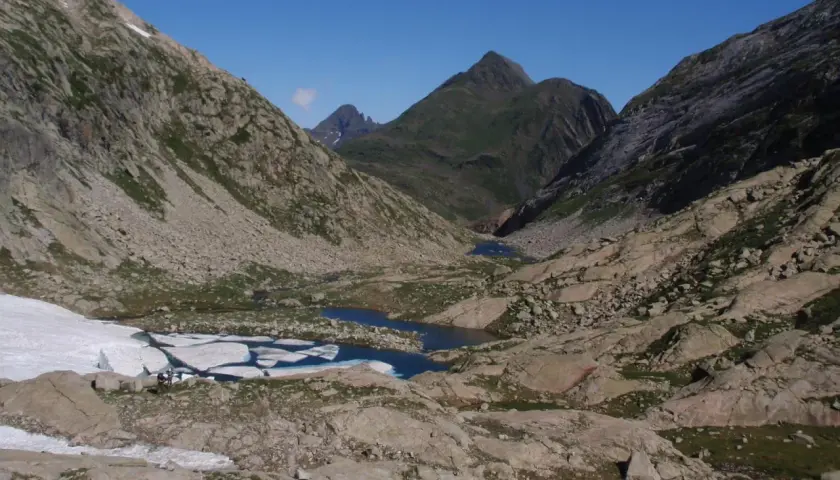 Paisaje de montaña con lagos glaciares y restos de nieve. El pico Mulleres se alza majestuoso en el horizonte.