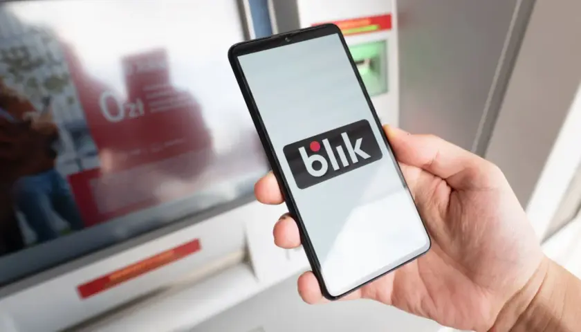 Dłoń trzyma smartfon z logo Blik. Czy Blik jest tylko w Polsce? Płatność zbliżeniowa przy bankomacie.