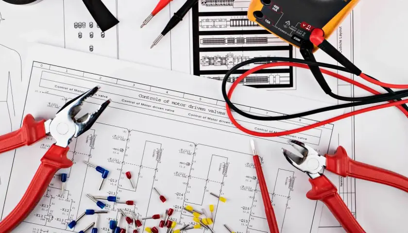 Narzędzia i schemat instalacji elektrycznej w domu. Multimetr, kombinerki i złączki czekają na montaż.