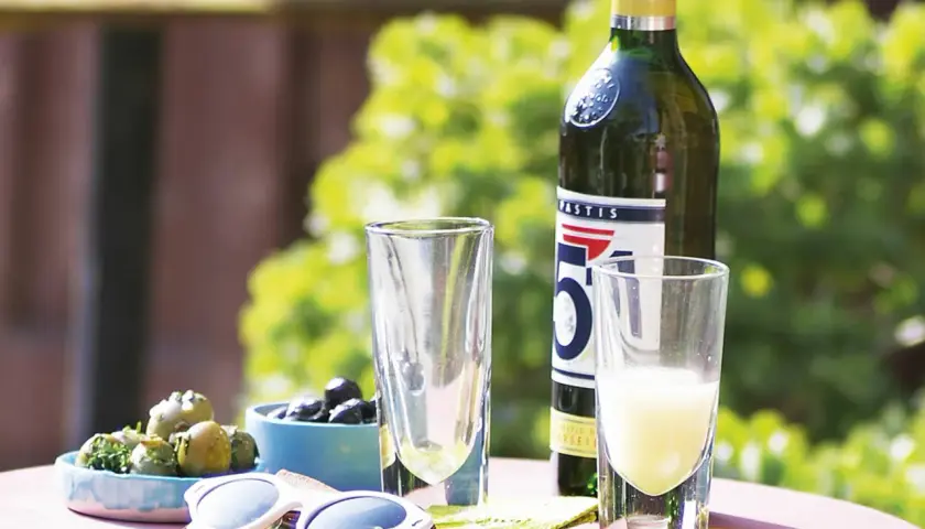 Ein Glas Pastis mit Anis Geschmack, Oliven und Sonnenbrille auf einem Tisch im Freien.