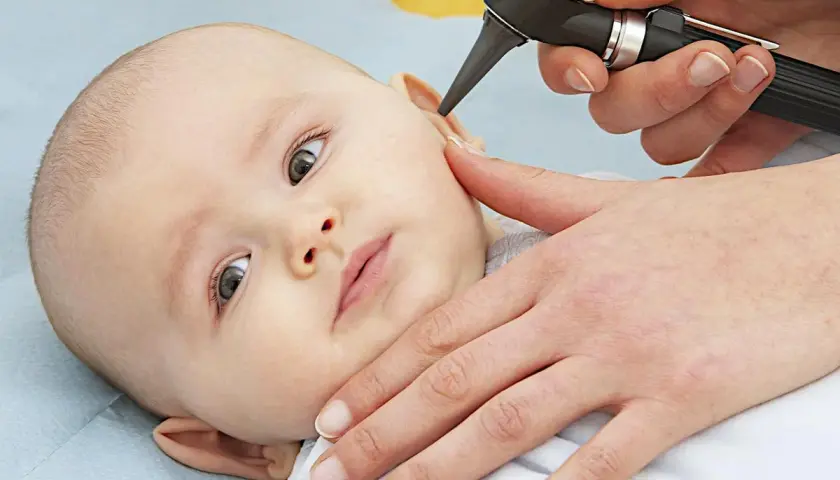 Un medico esamina l'orecchio di un neonato con un otoscopio. È importante controllare i bambini per l'otite.