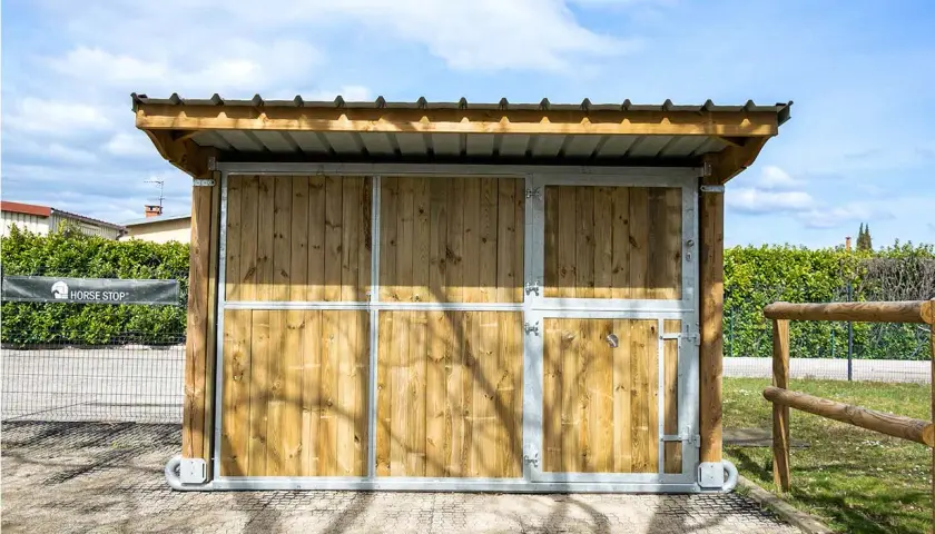 Ein mobiler Pferdestall ohne Baugenehmigung, aus Holz und Metall, mit Dach und Türen, ideal für flexible Pferdeunterbringung.