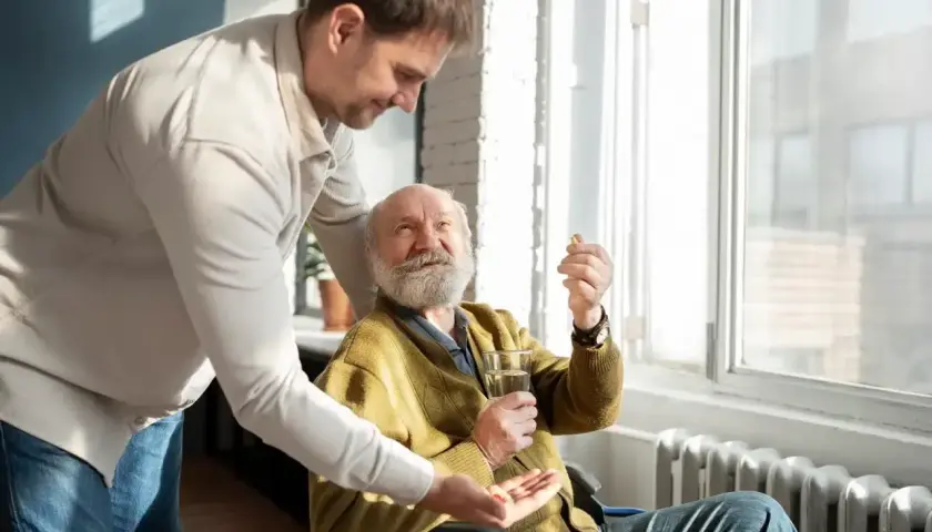 Mężczyzna podaje tabletki starszemu mężczyźnie na wózku inwalidzkim.