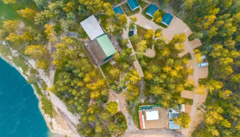 Malowniczy camping w Małopolsce nad turkusową wodą. Domyki, budynki i samochody wśród jesiennych drzew.