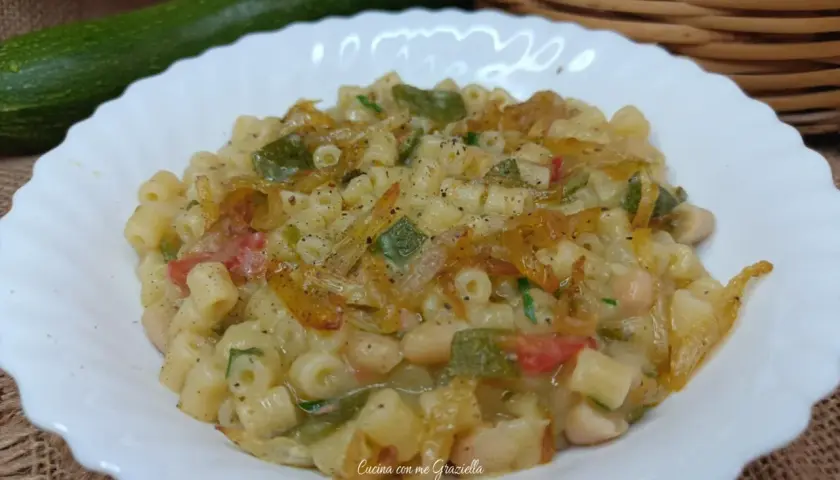 Un piatto invitante di pasta e zucchine alla pugliese, con fagioli e pomodoro, condito con erbe aromatiche.