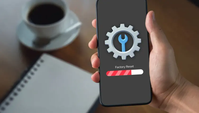 Dłoń trzyma telefon z ekranem pokazującym ikonę koła zębatego i klucza, oraz pasek postępu "Factory Reset". To rozwiązanie, jak zresetować telefon gdy nie działa dotyk.