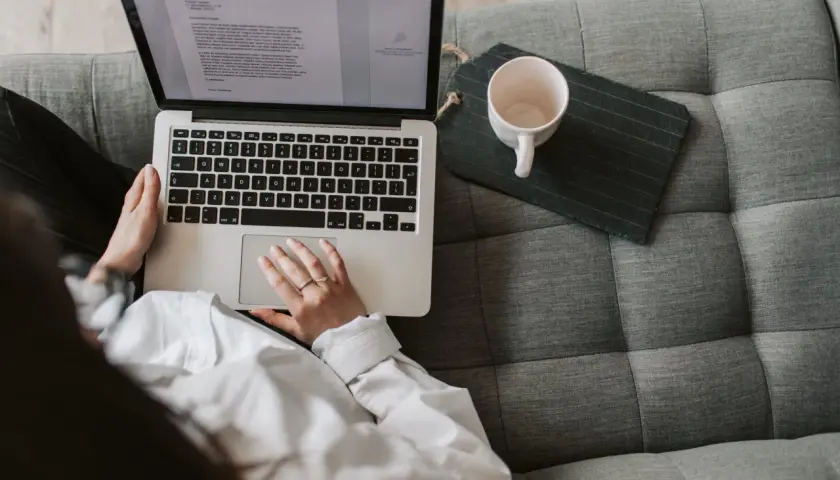 Scenarzysta pracuje nad nowym tekstem na laptopie, siedząc wygodnie na kanapie. Obok leży pusta filiżanka.