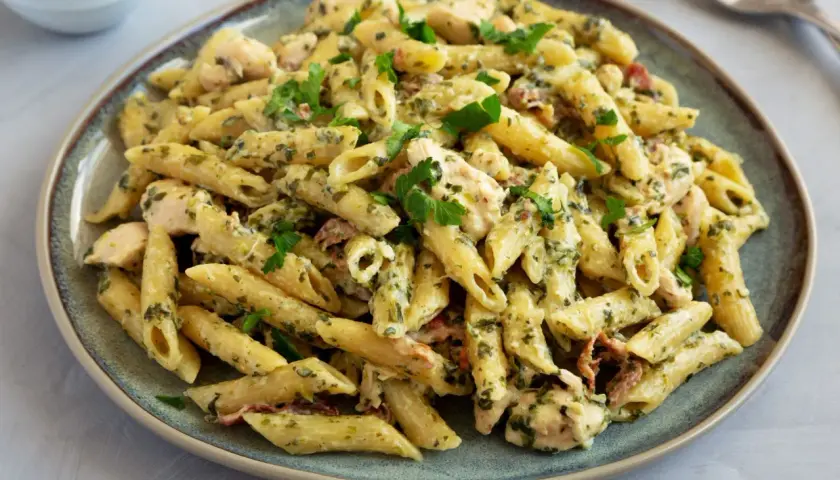 Kremowy makaron penne z kurczakiem, szpinakiem i suszonymi pomidorami, udekorowany natką pietruszki.