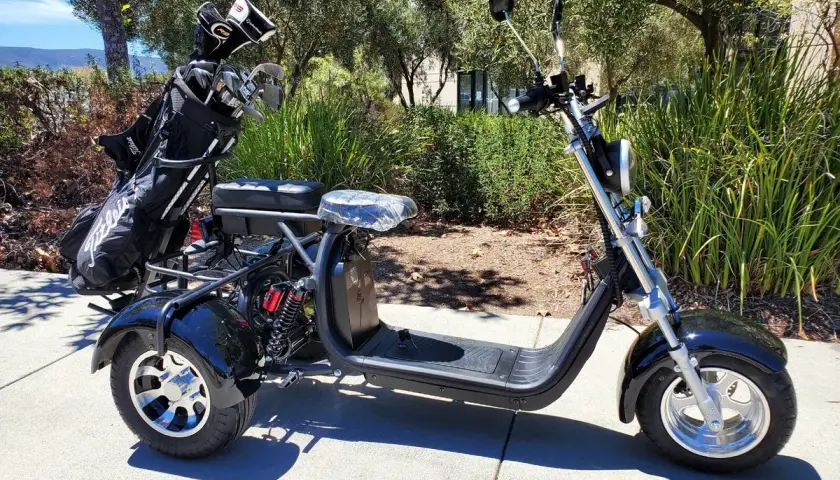 Trike negro de 3 ruedas con bolsa de golf en la parte trasera, aparcado en una acera.
