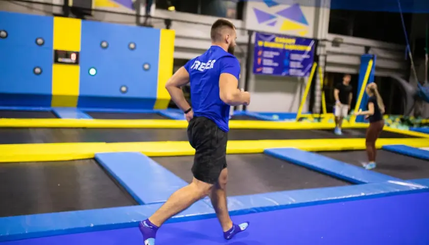 Mężczyzna w niebieskiej koszulce wykonuje trening interwałowy na trampolinach.