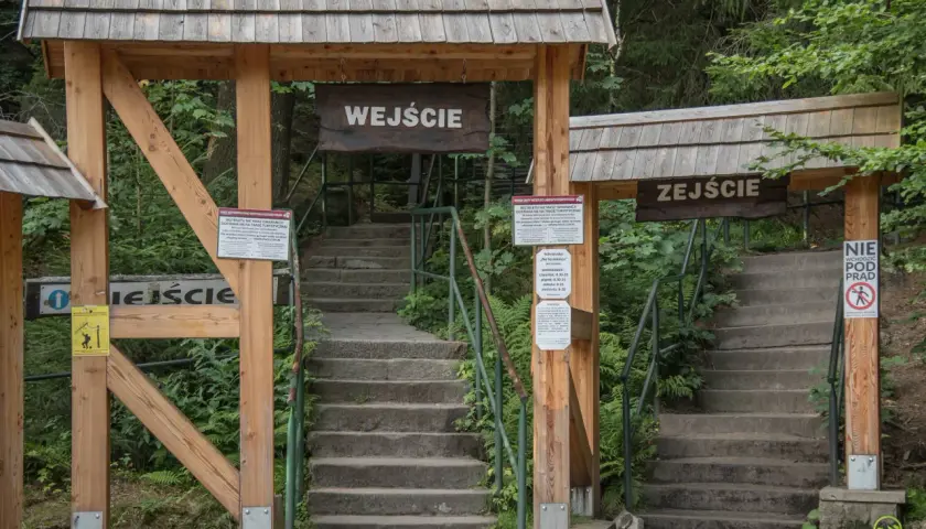 Kamienne schody prowadzą do wejścia na **Szczeliniec Wielki**. Drewniane bramy z tablicami informacyjnymi zapraszają do zwiedzania.