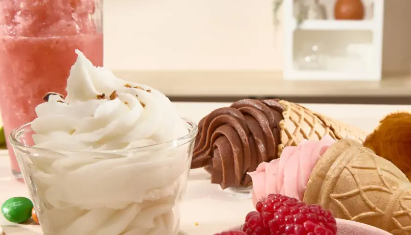 Un bicchiere di gelato sorbetto bianco, coni con gelato al cioccolato e fragola, lamponi freschi e una granita rosa.