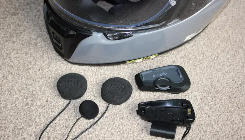 Akcesoria do interkomu motocyklowego Cardo i słuchawki JBL leżą obok kasku. Dowiedz się, jak zamontować interkom do kasku.
