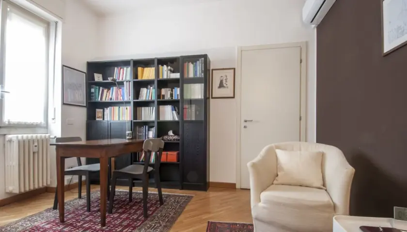 Arredamento accogliente per uno studio di psicoterapia: poltrona comoda, libreria piena e un tavolo per le sedute.