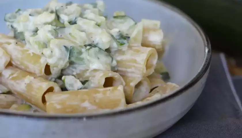 Pasta con calabacín cremosa, servida en un cuenco. Los trozos de calabacín se mezclan con la pasta y una salsa blanca.