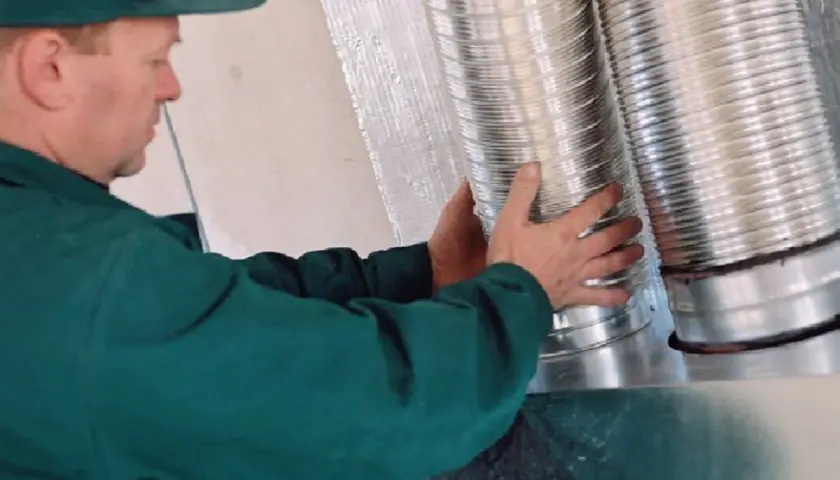 Instalator montuje rury do rozprowadzenia ciepłego powietrza z kominka.
