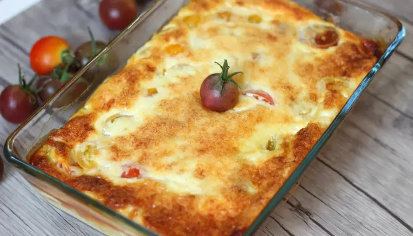 Un clafoutis tomates cerises doré et appétissant, garni d'une tomate cerise fraîche, prêt à être dégusté.