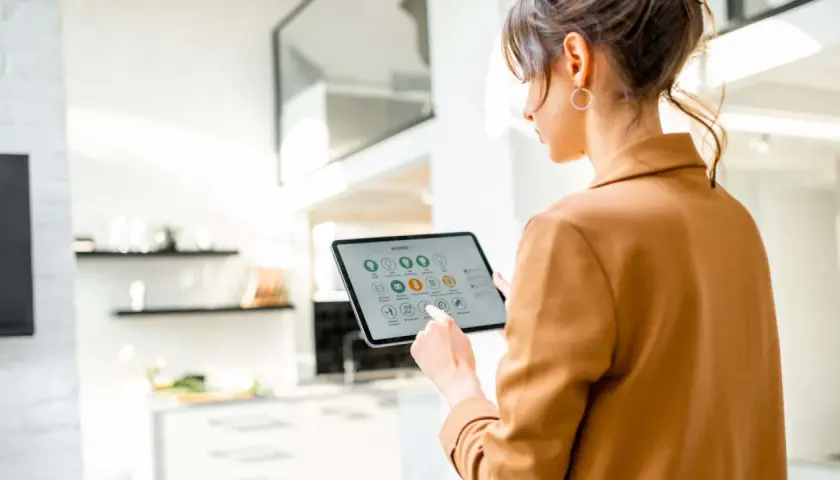 Mujer interactúa con una tablet que muestra la interfaz de un smart gateway para controlar su hogar inteligente.