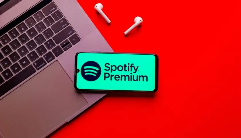 Laptop, telefon z logo Spotify Premium i słuchawki na czerwonym tle.