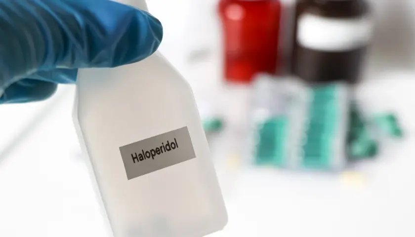 Blauer Handschuh hält Flasche mit der Aufschrift "Haloperidol". Im Hintergrund sind Medikamentenpackungen zu sehen.