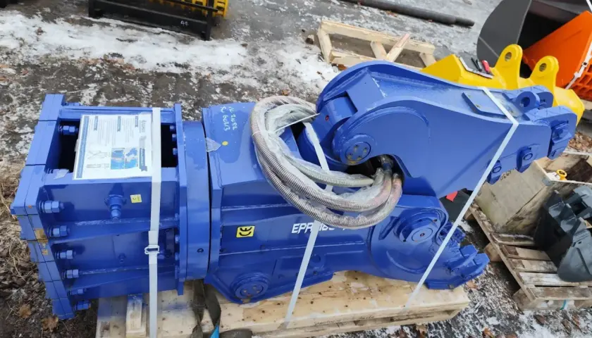 Solidne nożyce hydrauliczne do koparki, gotowe do pracy. W tle żółte i pomarańczowe łyżki.