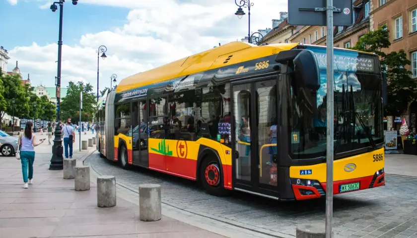 Żółto-czerwony autobus miejski, symbol darmowej komunikacji miejskiej, jedzie ulicą.