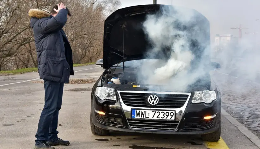 Mężczyzna zrezygnowany patrzy na dym spod maski i czuje zapach spalenizny. Awaria Volkswagena na poboczu.