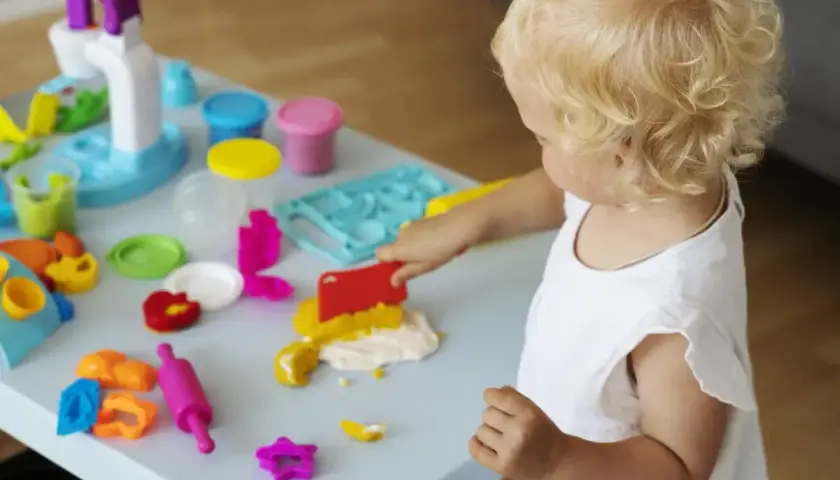 Mała blondynka w żłobku tworzy cuda z plasteliny. Wesołe zabawy sensoryczne rozwijają jej kreatywność.