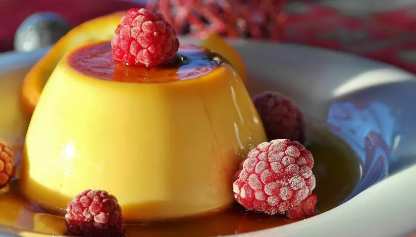 Crème aux œufs onctueuse, nappée de caramel et garnie de framboises givrées. Un délice visuel et gustatif.