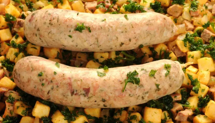 Deux andouillettes au four, dorées et savoureuses, reposent sur un lit de pommes de terre sautées et de persil frais. Un plat réconfortant prêt à être dégusté.