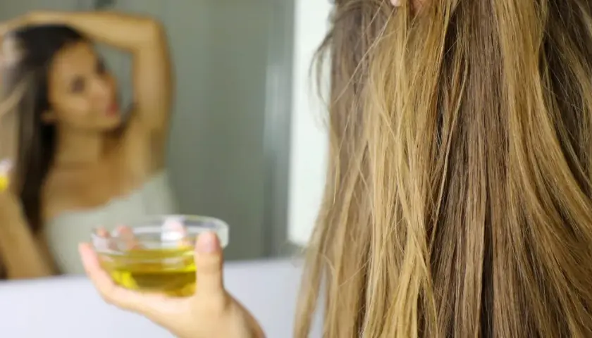 Mujer se aplica aceite de oliva en el cabello, demostrando que el aceite de oliva es bueno para el pelo.