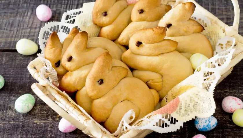 Korb voller goldbrauner Quark Osterhasen, umgeben von bunten Ostereiern auf dunklem Holz.