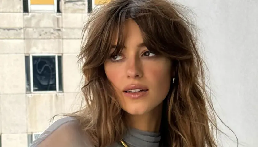 Mujer con flequillo cortina desfilado, cabello castaño ondulado y mirada pensativa.