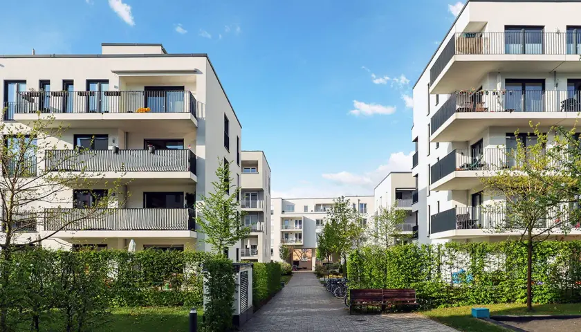 Immeubles modernes avec balcons, chemin pavé, verdure. Une location avec promesse de vente, un lieu de vie prometteur.
