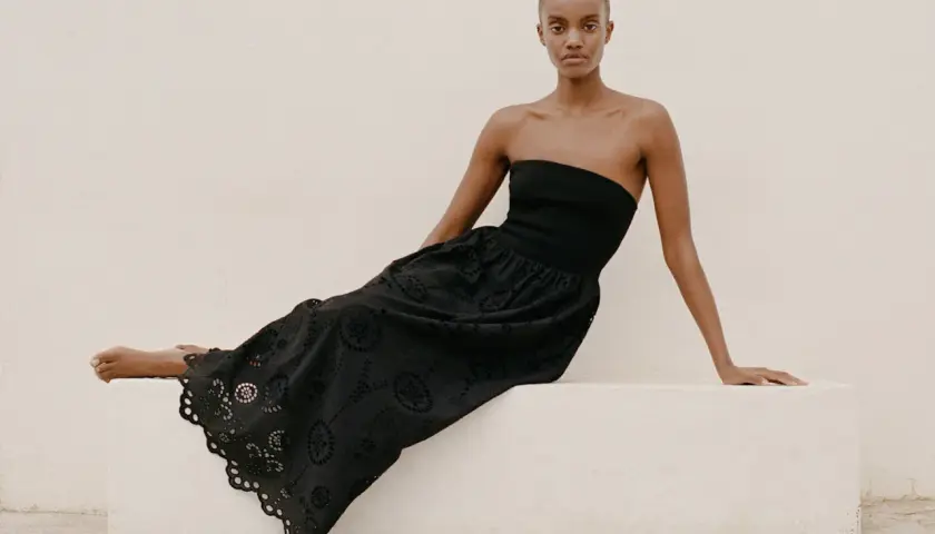 Mujer con vestido negro sin tirantes y falda larga con bordados florales, un ejemplo de moda ecológica.