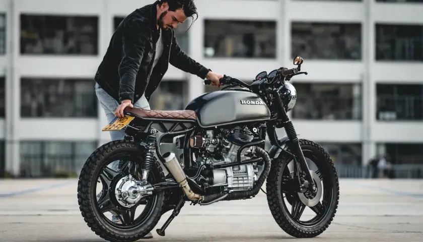 Uomo con moto custom grigia. La sella in pelle marrone ha una **godronatura** a rombi.