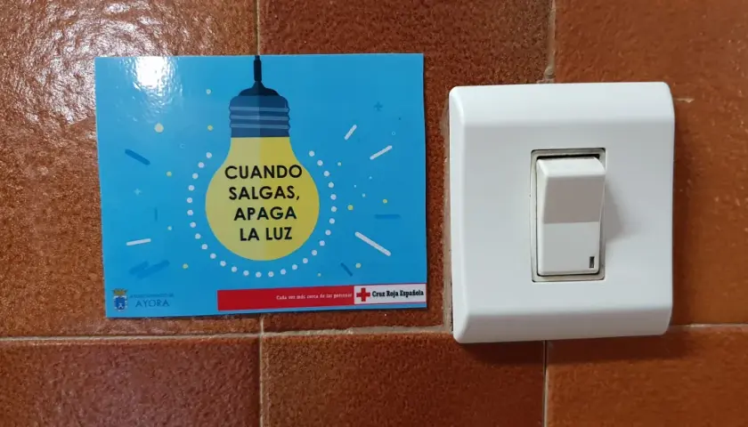 Un cartel azul con una bombilla amarilla y el texto "CUANDO SALGAS, APAGA LA LUZ" junto a un interruptor blanco.