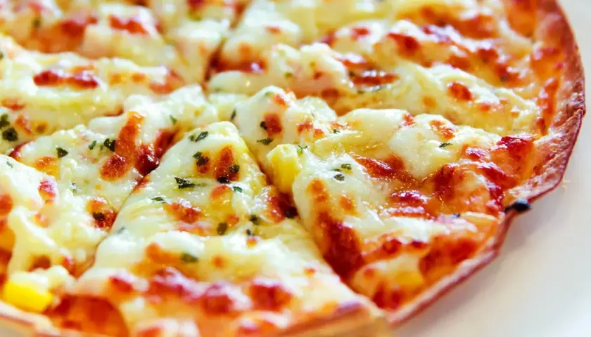 Pyszna pizza z tortilli, obficie posypana serem i ziołami, pokrojona na trójkątne kawałki.