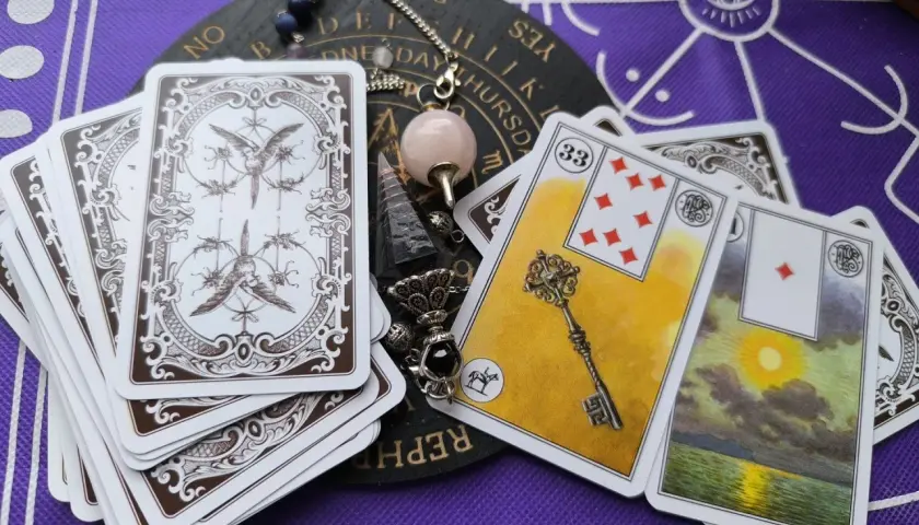 Odkryj znaczenie kart Lenormand. Na stole leżą karty, pendel i talizmany, gotowe do wróżenia.