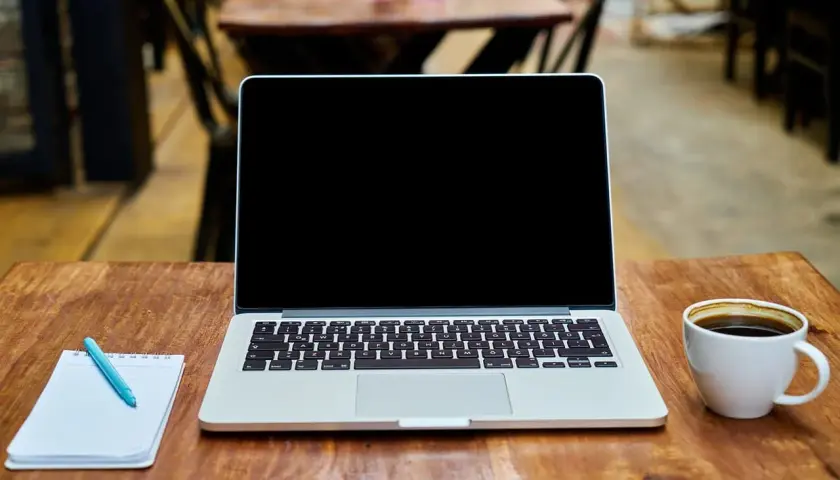 Laptop z pustym ekranem, notatnik z długopisem i filiżanka kawy na drewnianym stole. Idealne miejsce do pracy nad projektem z wykorzystaniem dysku hybrydowego.