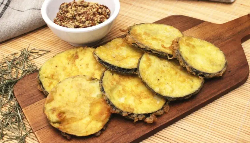 Berenjenas rebozadas doradas y crujientes, servidas en tabla de madera con un cuenco de mostaza.