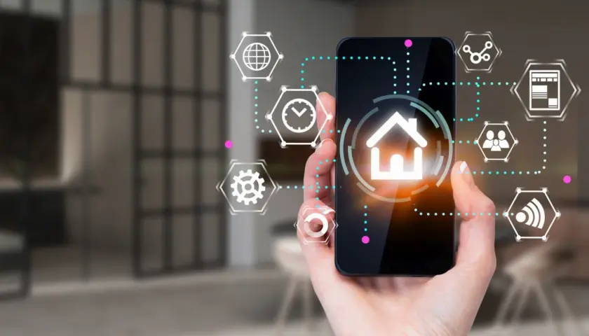 Dłoń trzyma smartfon z ikoną domu i otaczającymi go symbolami. To interfejs aplikacji spectrum smart, zarządzającej inteligentnym domem.