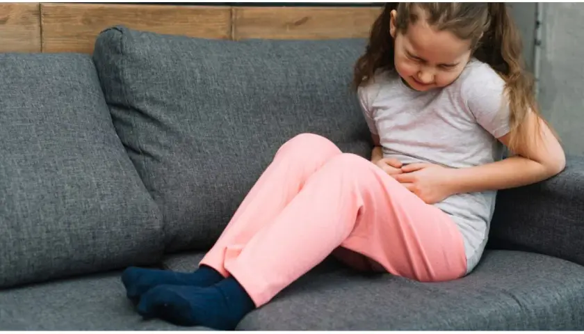 Bambina sul divano con le mani sulla pancia, che mostra i sintomi di appendicite.