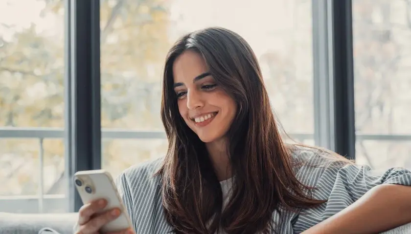 Uśmiechnięta kobieta trzyma telefon, czeka na wiadomość od ukochanej osoby. To piękny przykład, jak technologia wspiera związek na odległość.
