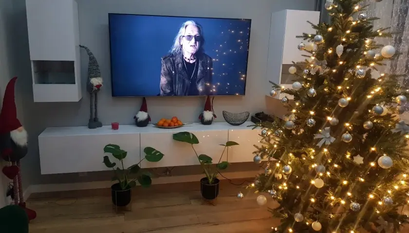 Świąteczny nastrój w domu: choinka, ozdoby, krasnale i telewizor z koncertem.