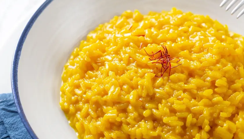 Risotto alla Milanese, un classico tra i piatti tipici lombardi, cremoso e profumato allo zafferano, guarnito con pistilli rossi.