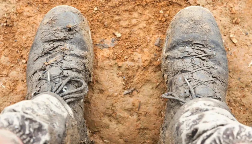 Mud-caked boots stand in dirt. The question "do boots shrink over time?" lingers as these boots look like they've seen many adventures.