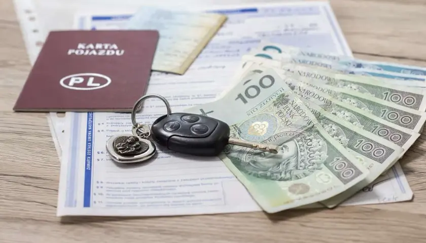 Karta pojazdu, kluczyki i polskie banknoty 100 zł leżą na dokumentach. Gotowy do zakupu lub sprzedaży samochodu.