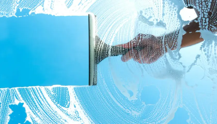 Mano con tergivetro crea strisce di schiuma su un vetro azzurro, per una perfetta pulizia finestre.